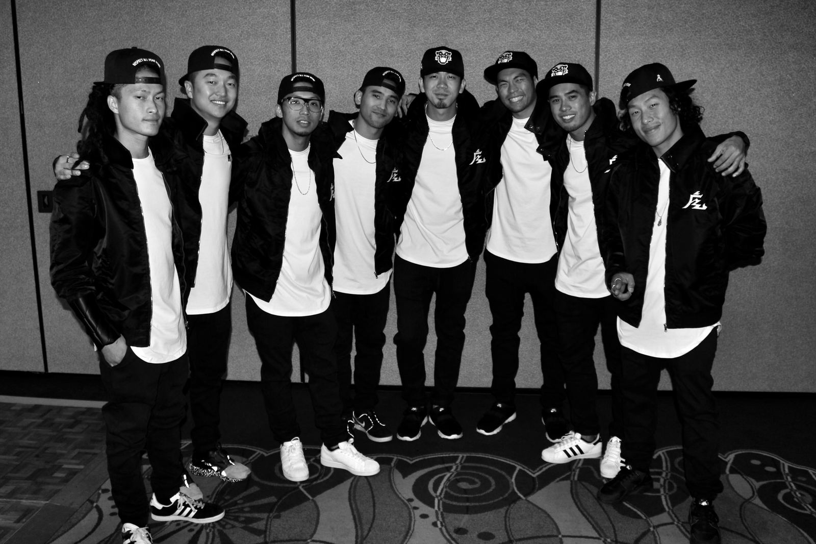 The Kinjaz crew lined up in black jackets and caps, black and white