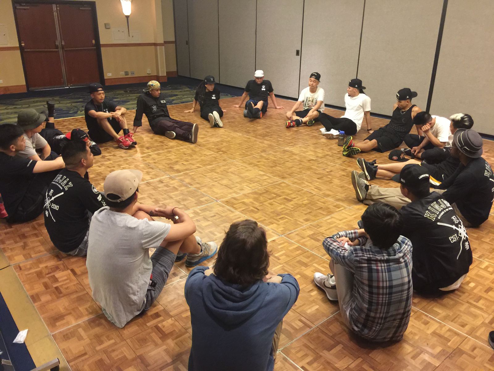 The crew sitting in a circle on a ballroom floor during rehearsal