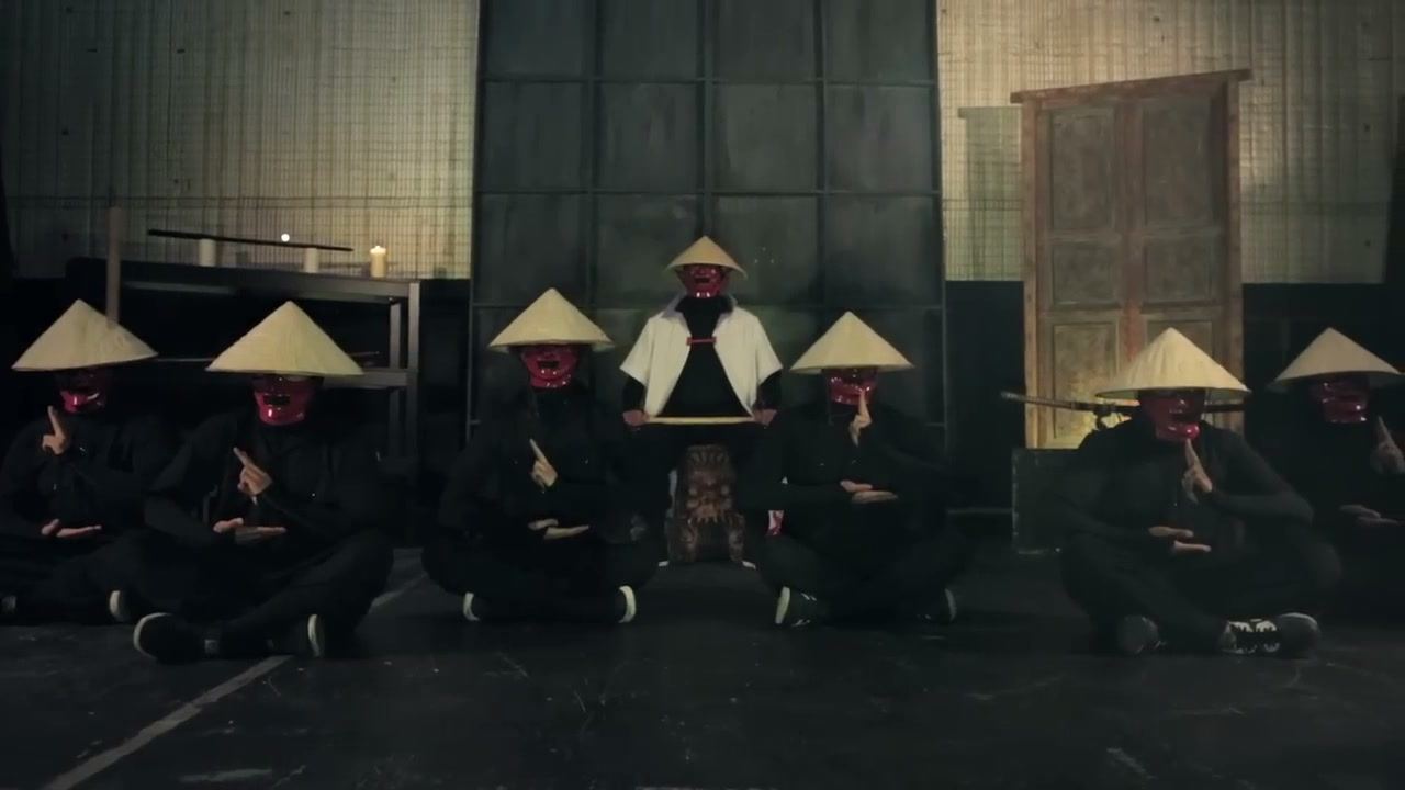 Kinjaz members in rice hats and red masks, seated in a dark room, from the 2012 video