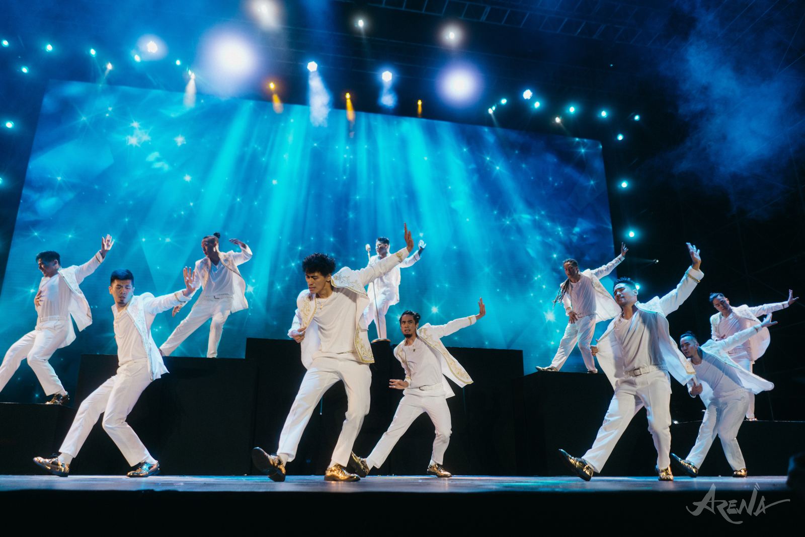 Dancers in white on a blue-lit stage at Arena