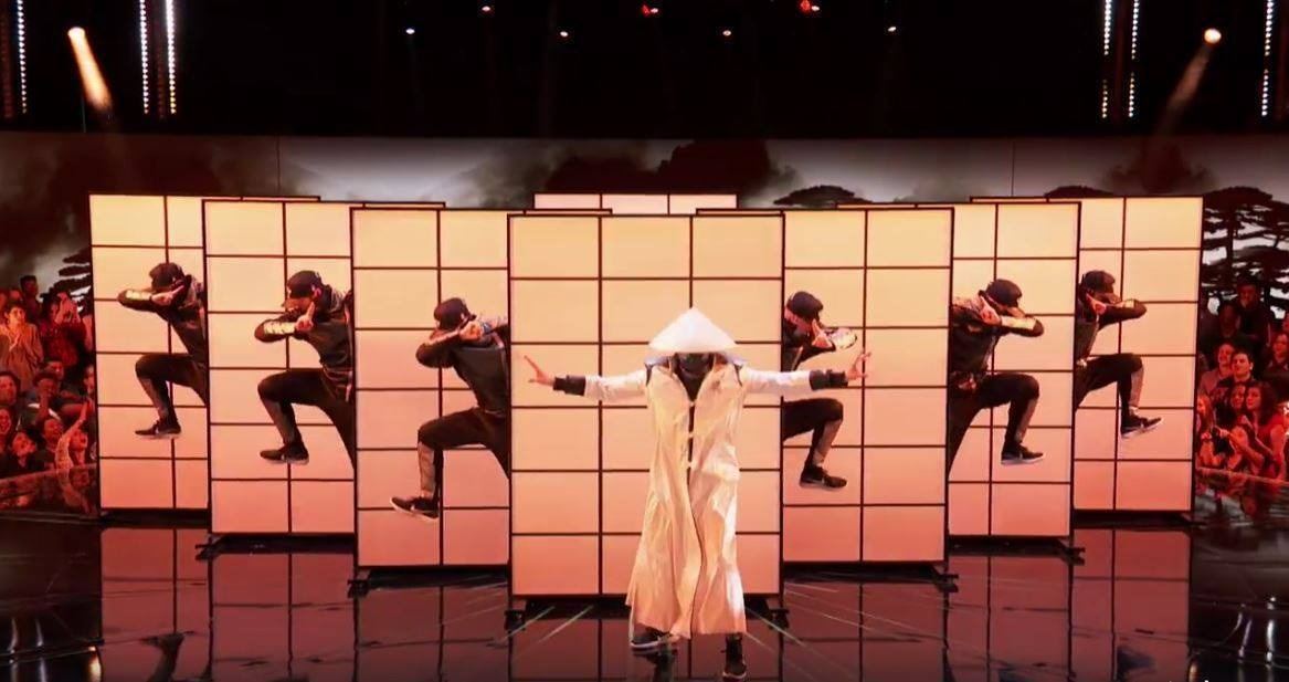 Dancers in lit panels behind a figure in a rice hat on the World of Dance stage